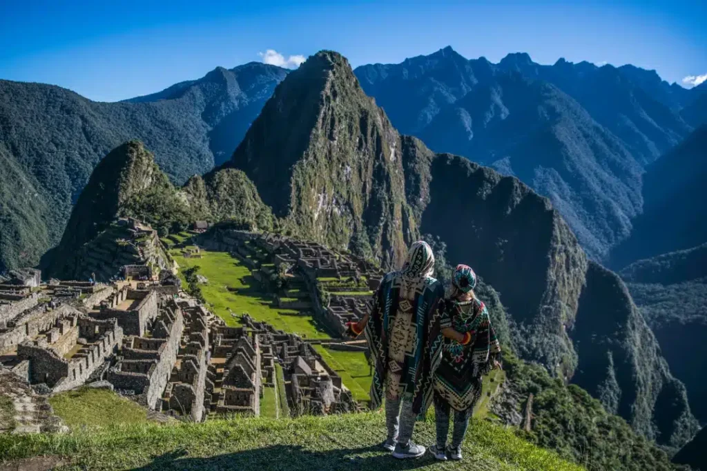 Travelers in traditional Andean clothing overlooking Machu Picchu from the Sun Gate, framed by green terraces and Huayna Picchu – Peru Hikers