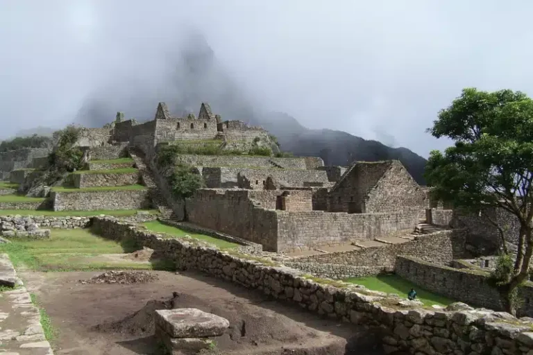 Panoramic view of Machu Picchu's ancient stone buildings and terraces on a misty morning, the iconic end of the classic inca trail - Peru Hikers.