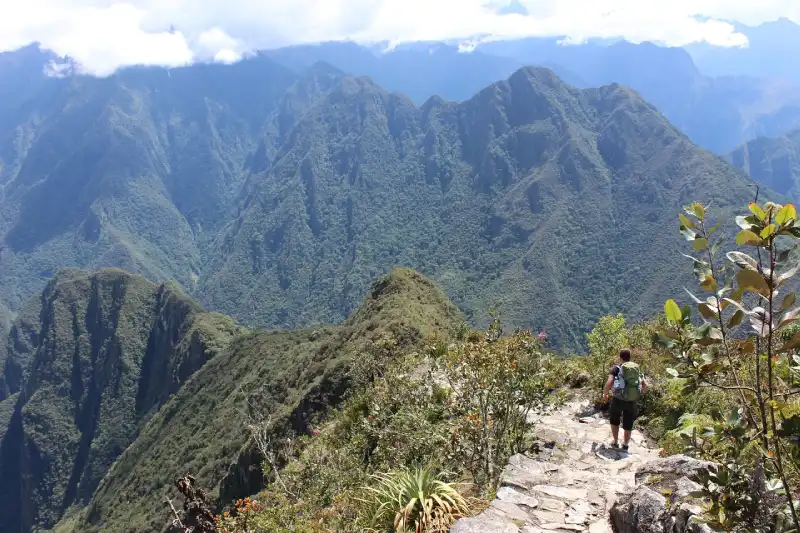 Hiker on a mountain trail overlooking the lush Urubamba Valley and peaks near Machu Picchu, a landscape visible on or connecting to a Machu Picchu Vistadome day trip - Peru Hikers.