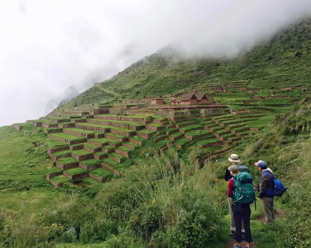 Three hikers observing Inca terraces and mist-covered mountains in the Sacred Valley, highlighting the historical depth of the Short Inca Trail – Peru Hikers