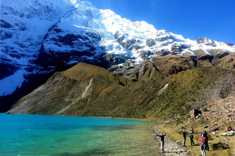 Tourists admiring the vibrant turquoise Humantay Lake with towering snow-capped mountains, a stunning sight on or near the Ausangate Trek - Peru Hikers.