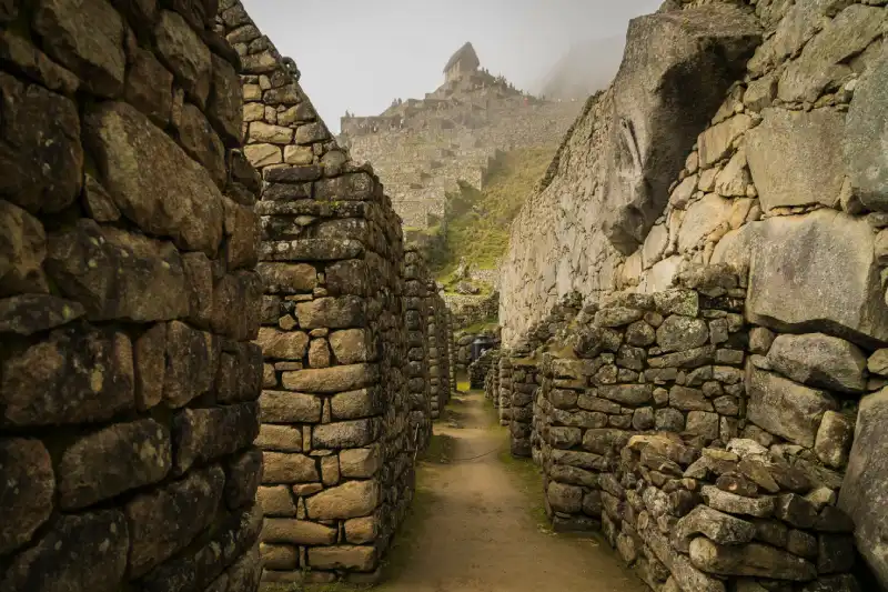 A narrow pathway winds through ancient stone walls within Machu Picchu, a key attraction for Cusco's visitors. - Peru Hikers
