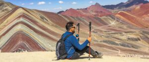 A person with hiking gear looking out at the panoramic view of the colorful, striped Rainbow Mountains, a rewarding scene on the Ausangate Trek. - Peru Hikers