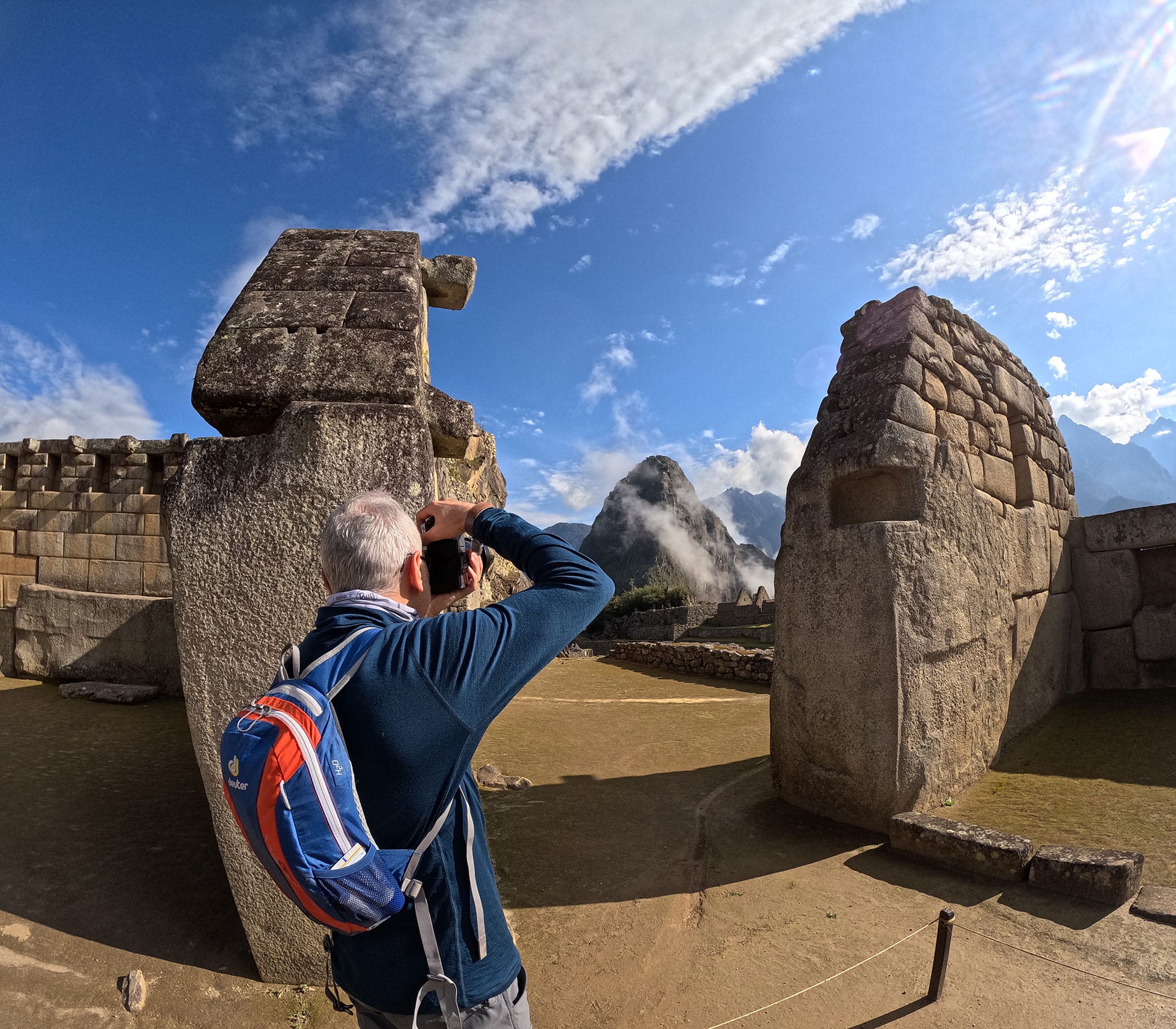 A person with a backpack taking a picture with a camera among the stone ruins of Machu Picchu, with mountains in the background, a common activity on a Machu Picchu Vistadome day trip. - Peru Hikers