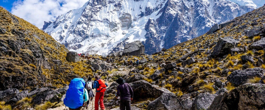 Trekkers on a rocky path with a glacier in the background, showcasing the dry conditions of the peak Peru travel seasons - Peru Hikers