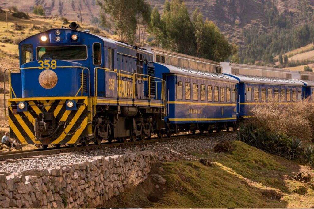 Blue and yellow PeruRail train crossing Andean landscape en route to Machu Picchu, symbolizing the journey toward the Huayna Picchu Hike – Peru Hikers