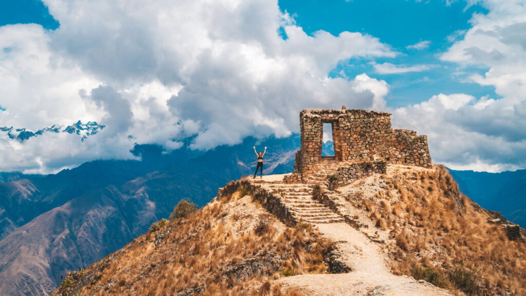 A hiker celebrates on a classic Inca Trail trek with ancient ruins and Andes mountains in the background.