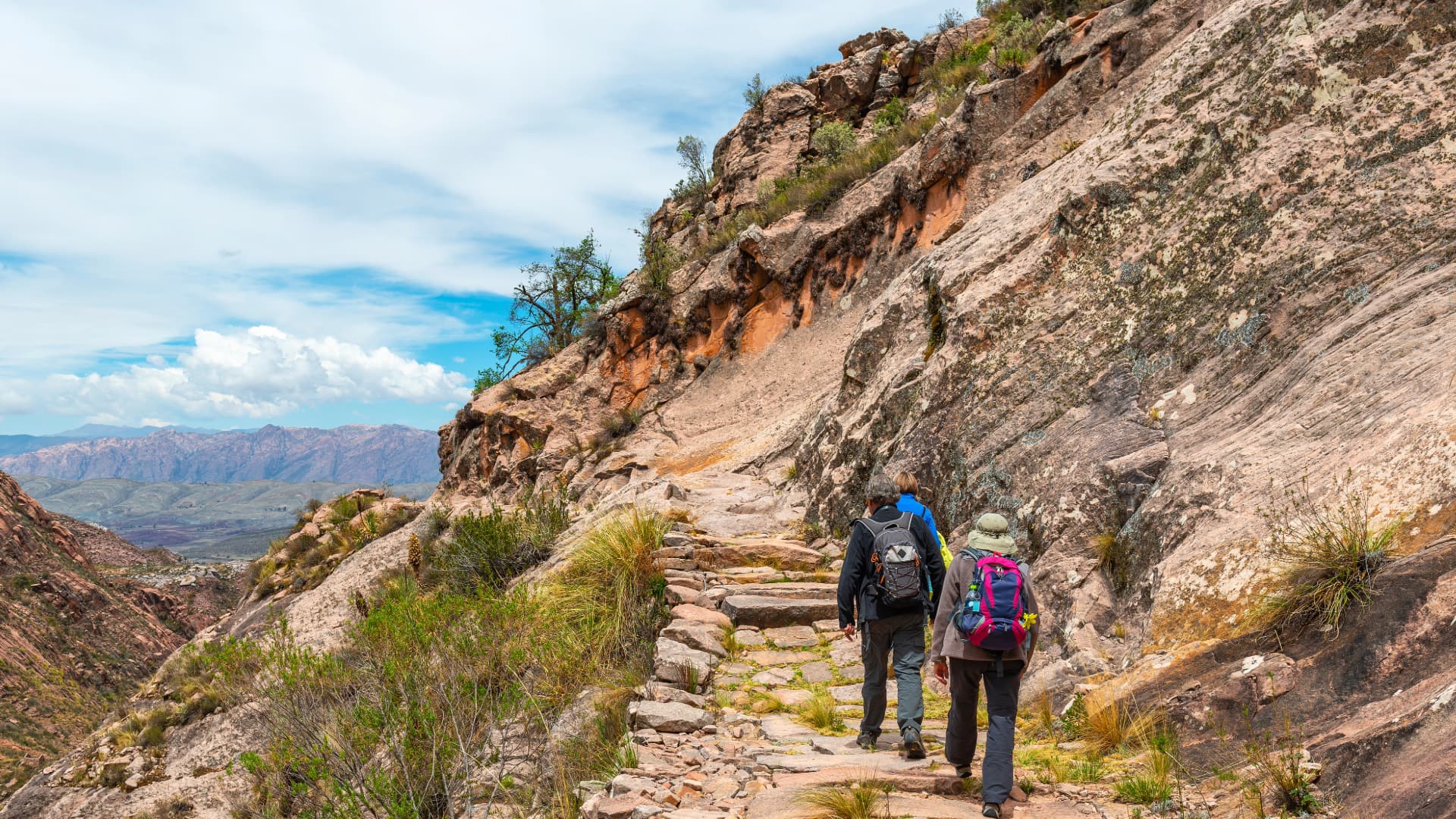 Two hikers walking along a rocky mountain trail on the Short Inca Trail for Beginners, surrounded by dramatic Andean terrain – Peru Hikers
