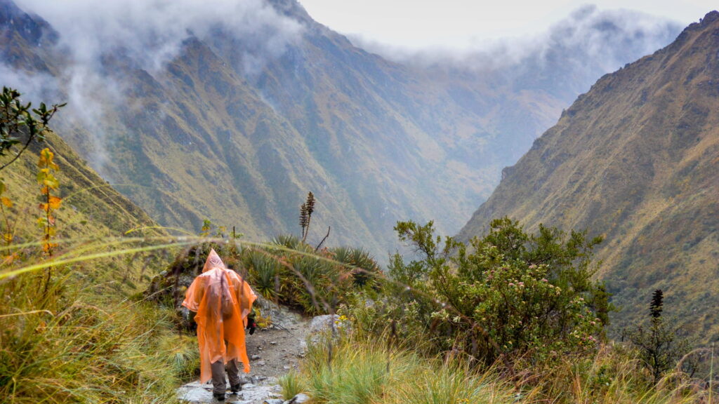 Hiker wearing a poncho on the Short Inca Trail during the rainy season, surrounded by lush green mountains and mist - Peru Hikers