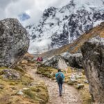 Hiker passing large glacial boulders on the alpine path, illustrating the challenging side of the salkantay trek vs lares trek - Peru Hikers